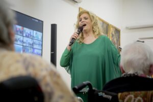 Iva Zanicchi all'interno di una RSA con il microfono in mano che canta