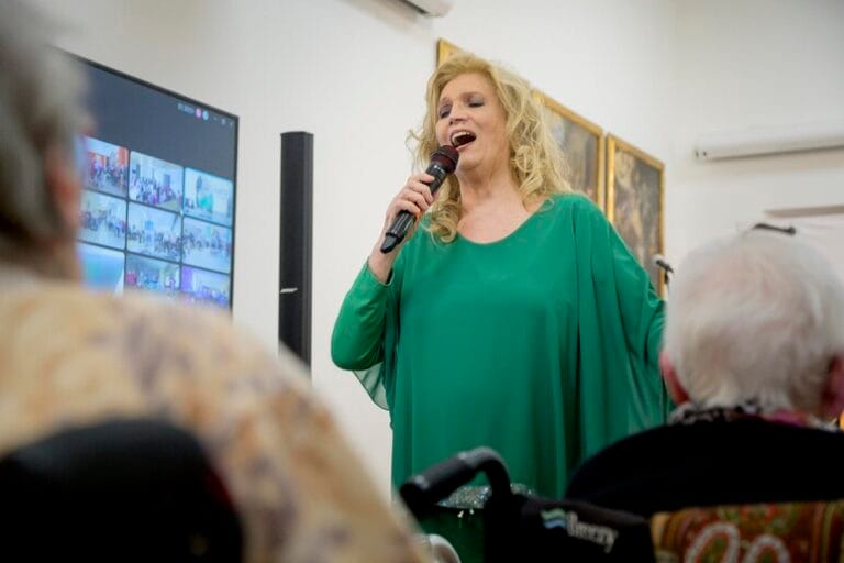 Iva Zanicchi all'interno di una RSA con il microfono in mano che canta